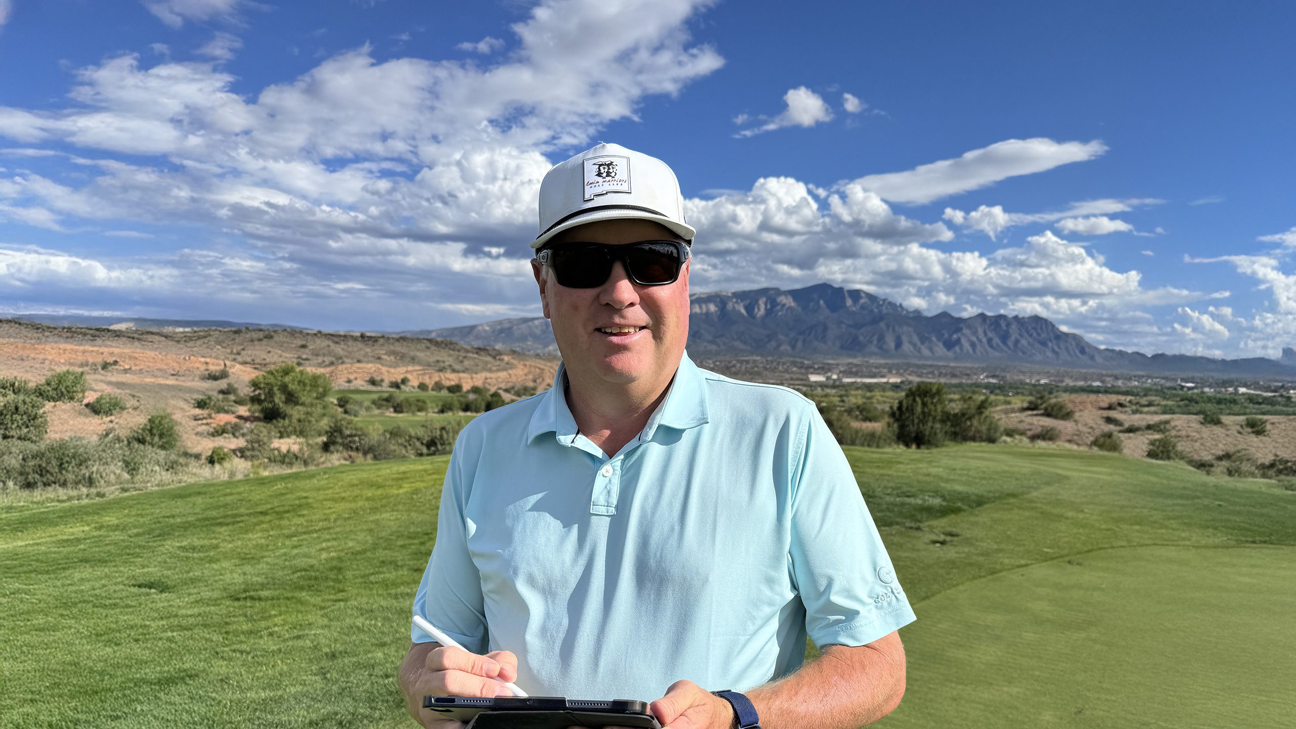 Gary Brawley using a tablet on a golf course with mountains in the background