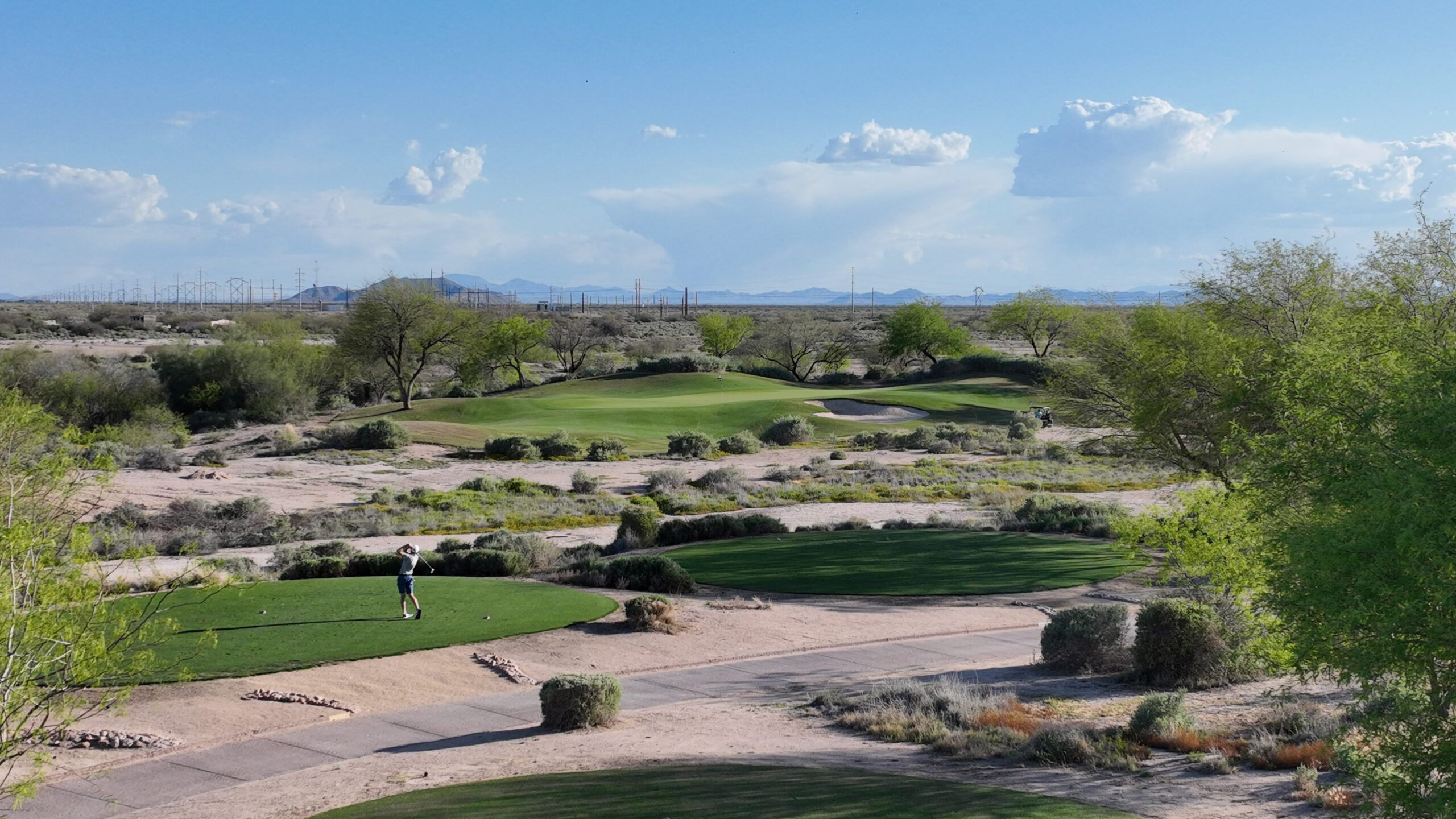 Golfer teeing off at Whirlwind Golf Club with desert terrain