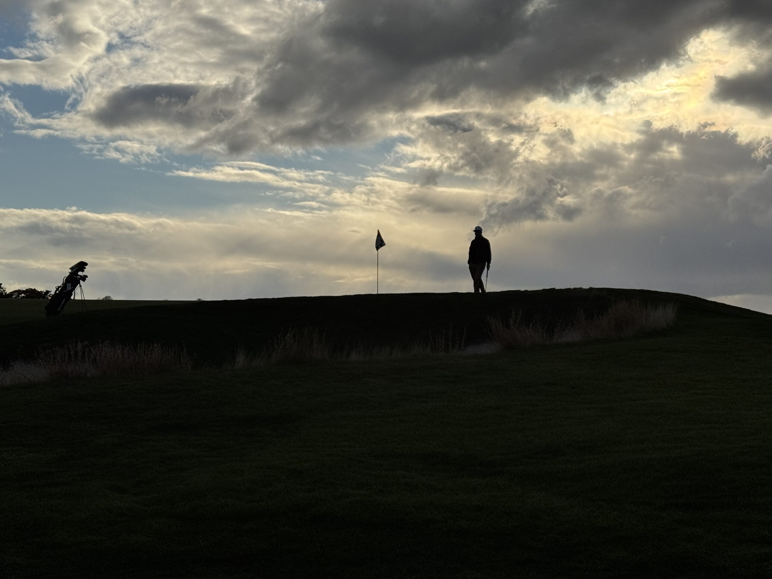 Golfer standing on a putting green near a flag with clouds overhead